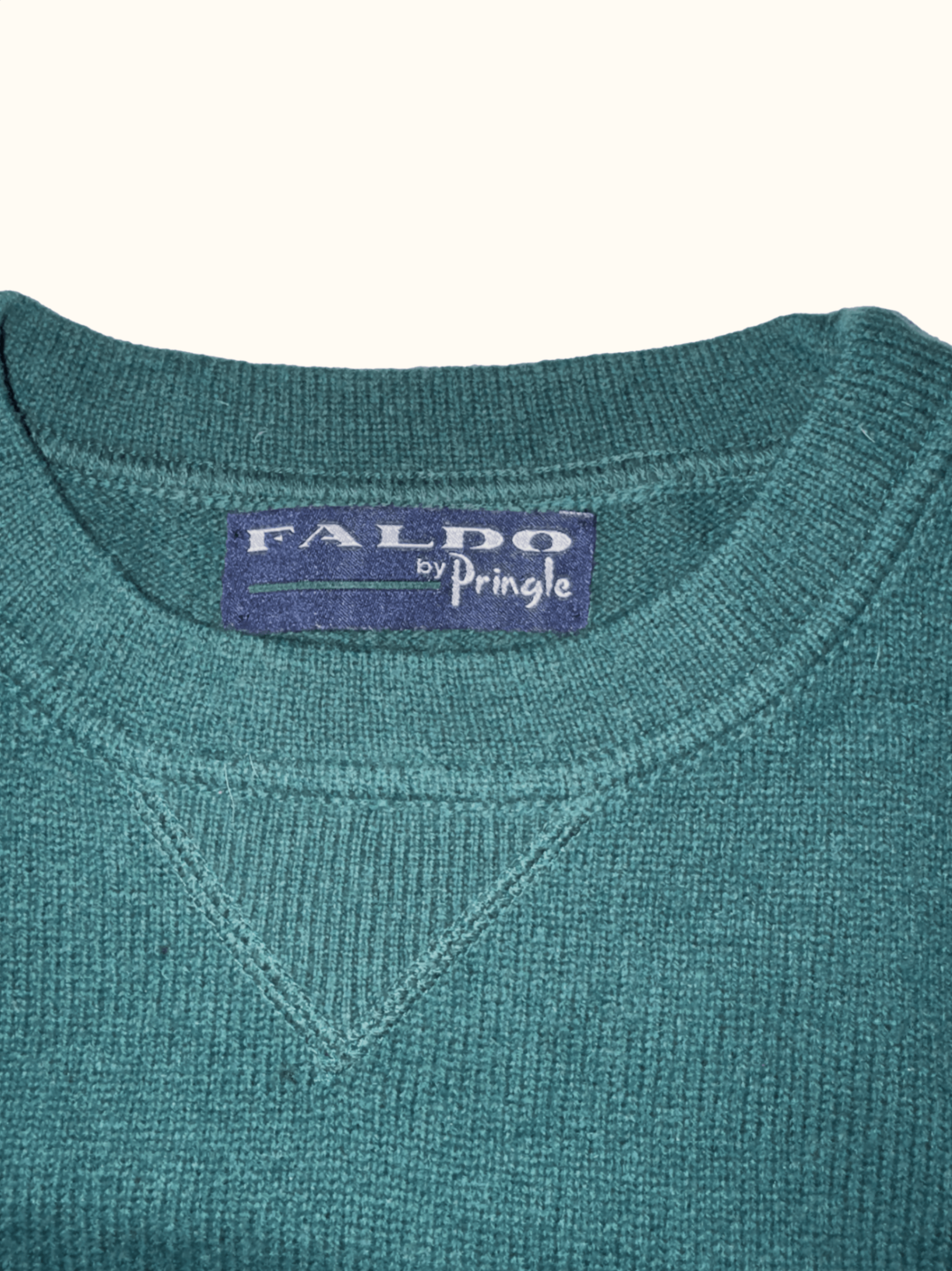 Close-up of a teal sweater with 'Faldo by Pringle' label on a white background